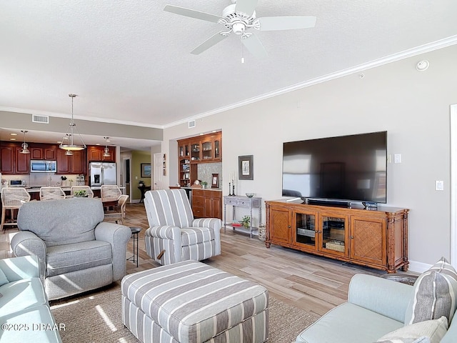 living room featuring visible vents, crown molding, light wood-type flooring, and a ceiling fan