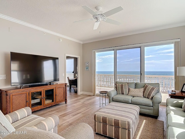 living area with a ceiling fan, a water view, a textured ceiling, crown molding, and light wood-type flooring