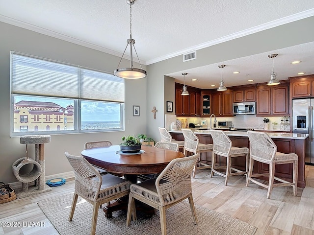 dining space featuring visible vents, baseboards, light wood-style flooring, ornamental molding, and a textured ceiling