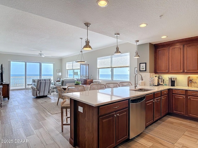 kitchen featuring a sink, a kitchen breakfast bar, stainless steel dishwasher, a peninsula, and light countertops