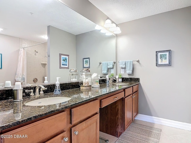 bathroom with a textured ceiling, double vanity, tiled shower, and a sink