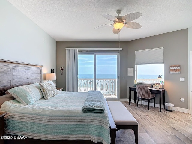 bedroom with multiple windows, a textured ceiling, wood finished floors, and access to outside