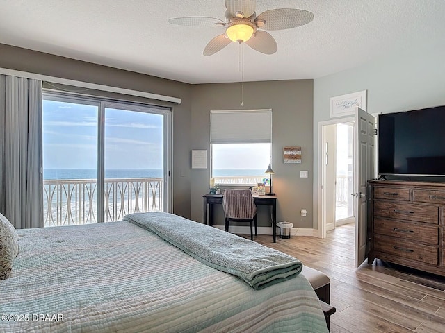 bedroom featuring wood finished floors, baseboards, access to exterior, a water view, and a textured ceiling