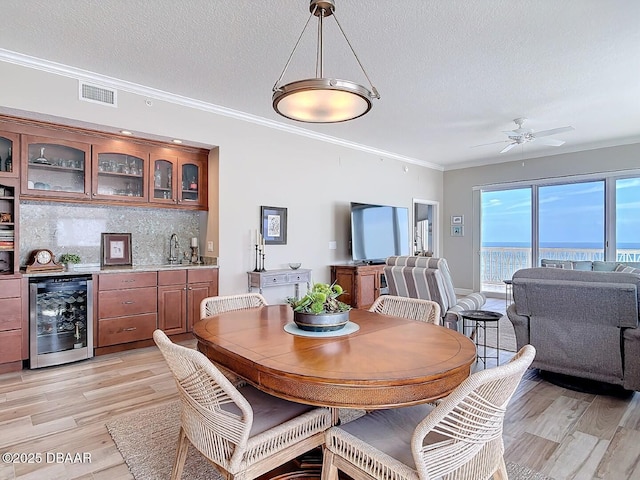 dining space with visible vents, wet bar, beverage cooler, and light wood-style flooring