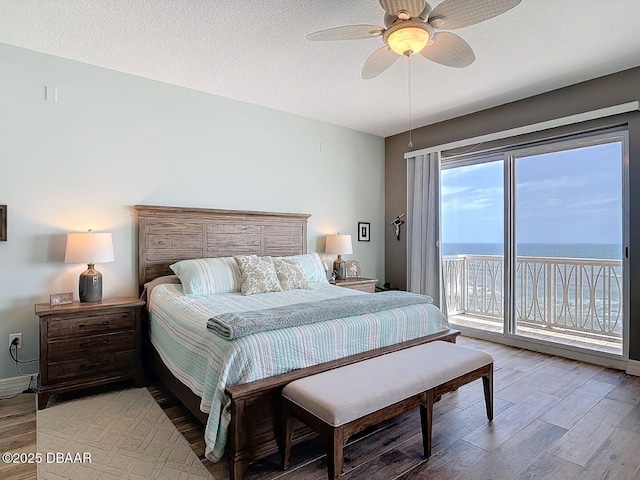 bedroom with ceiling fan, a water view, wood finished floors, a textured ceiling, and access to outside