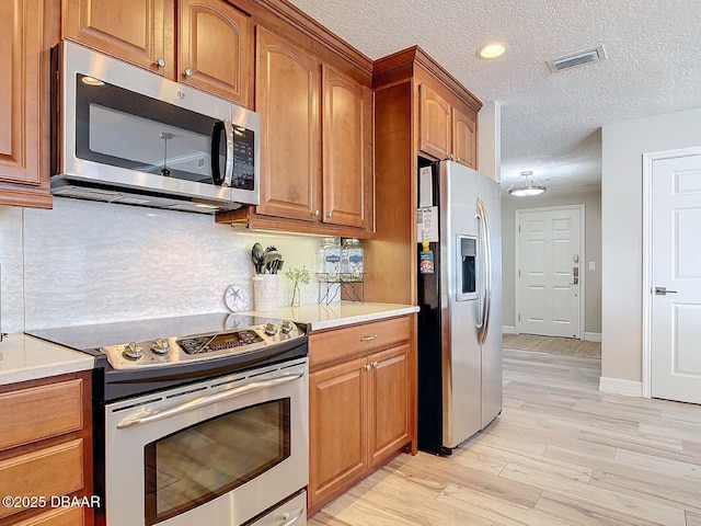 kitchen with visible vents, backsplash, stainless steel appliances, light wood-style floors, and brown cabinetry