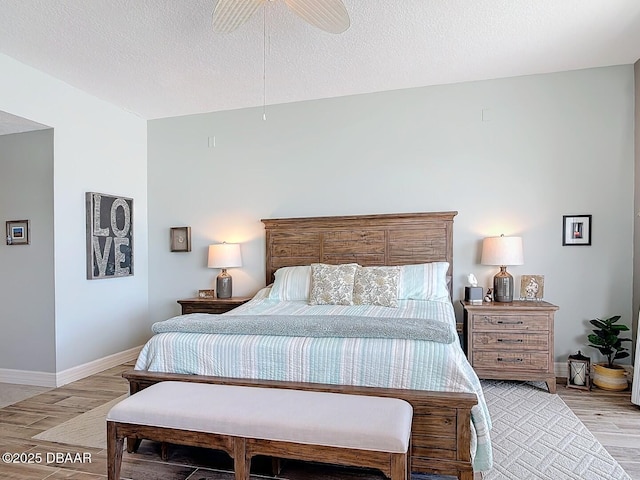 bedroom with ceiling fan, light wood-style flooring, baseboards, and a textured ceiling