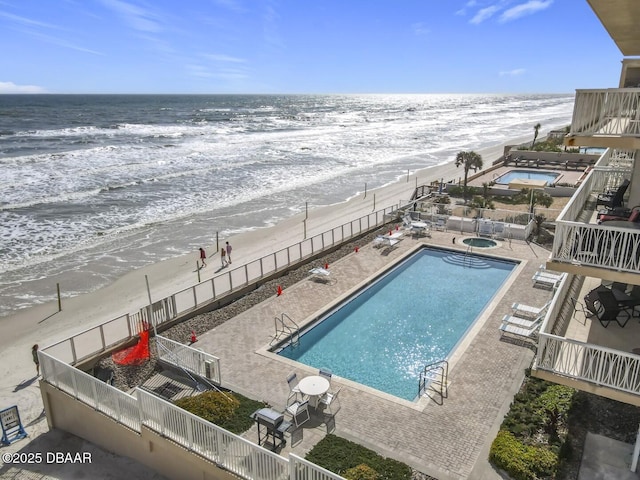 pool featuring a patio, a fenced backyard, a water view, and a beach view