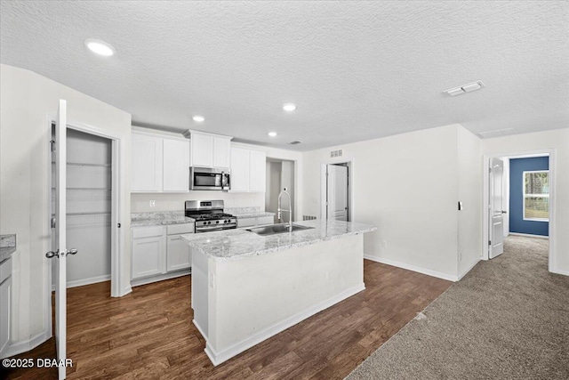 kitchen with sink, stainless steel appliances, light stone countertops, an island with sink, and white cabinets