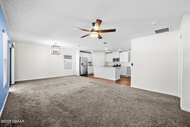 unfurnished living room featuring a textured ceiling, ceiling fan, and dark colored carpet