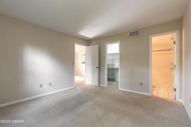 unfurnished bedroom featuring light colored carpet, a closet, connected bathroom, and a walk in closet