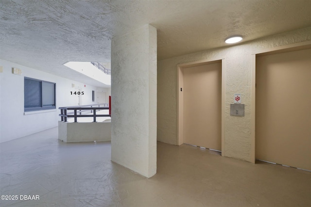 corridor featuring a textured wall, elevator, and a textured ceiling