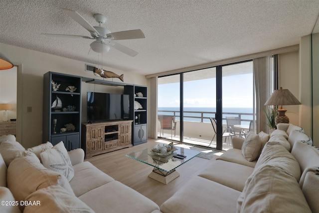 living room featuring ceiling fan, a wall of windows, light wood-style floors, a textured ceiling, and visible vents