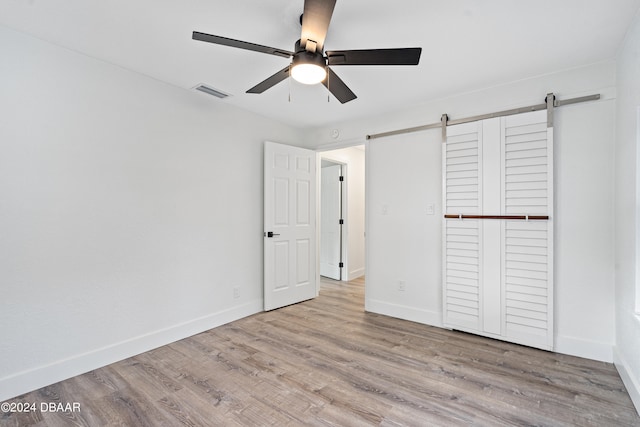 unfurnished bedroom featuring light wood-type flooring, a barn door, ceiling fan, and a closet