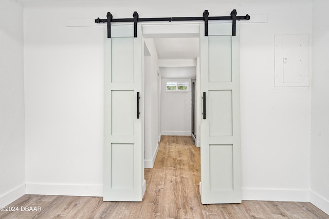 hallway with electric panel, a barn door, and light wood-type flooring