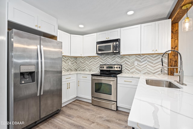 kitchen with sink, appliances with stainless steel finishes, hanging light fixtures, light hardwood / wood-style flooring, and white cabinets