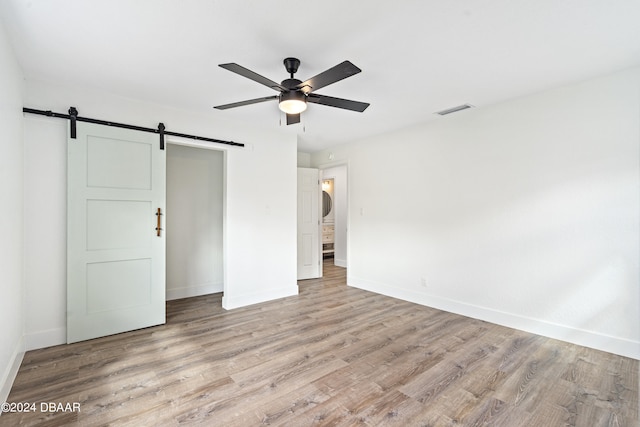 unfurnished room featuring a barn door, ceiling fan, and light hardwood / wood-style flooring