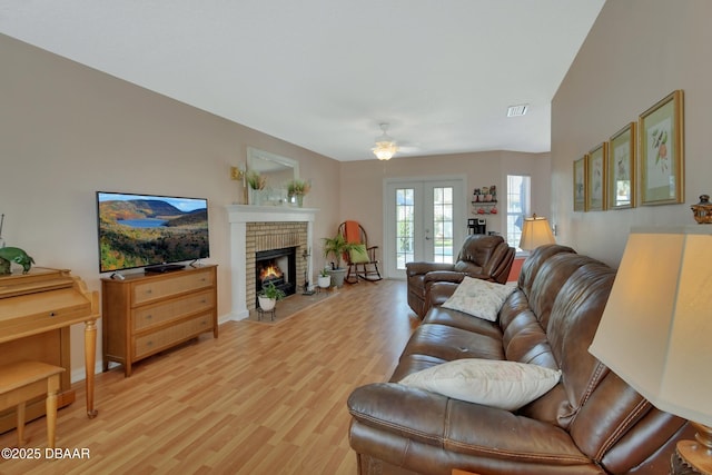 living room with light wood-type flooring, a brick fireplace, visible vents, and french doors