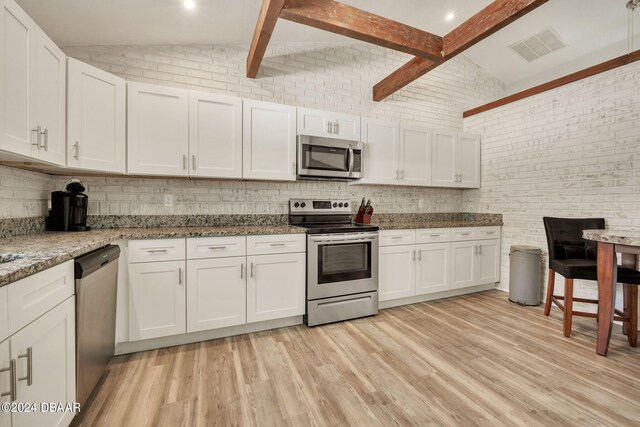 kitchen featuring stainless steel appliances, white cabinetry, and brick wall