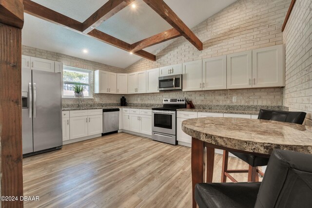 kitchen with stainless steel appliances, white cabinetry, vaulted ceiling with beams, and light wood-type flooring