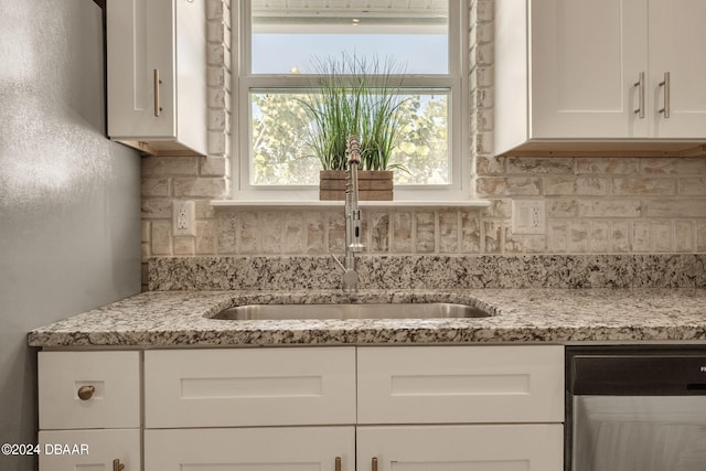 kitchen with tasteful backsplash, light stone countertops, sink, white cabinets, and stainless steel dishwasher