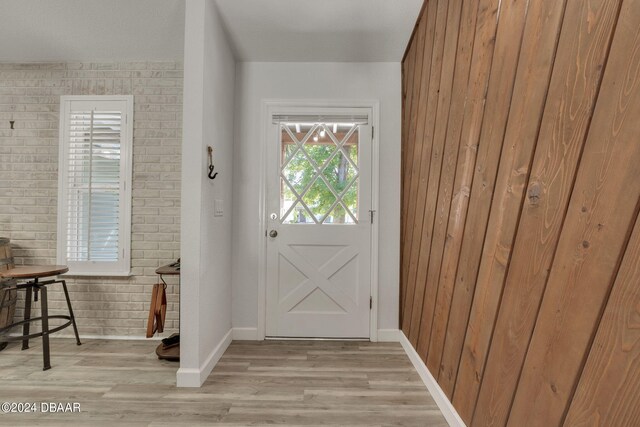 entryway with wood walls, brick wall, and light hardwood / wood-style flooring