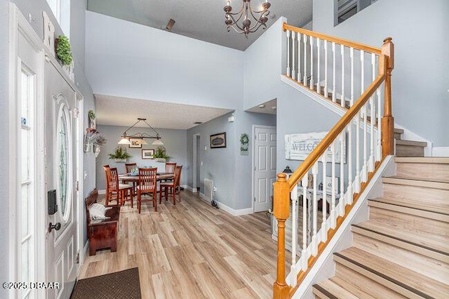 entryway with a towering ceiling, light hardwood / wood-style floors, and an inviting chandelier