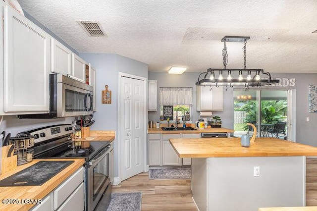 kitchen featuring a textured ceiling, stainless steel appliances, pendant lighting, white cabinets, and butcher block counters