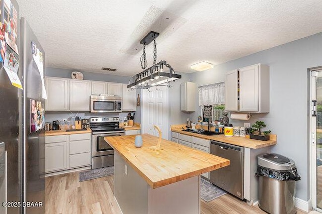 kitchen featuring butcher block countertops, a center island, a textured ceiling, and appliances with stainless steel finishes