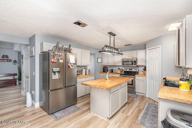 kitchen featuring white cabinets, stainless steel appliances, a kitchen island, and butcher block countertops