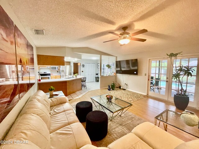 living room featuring light wood-type flooring, lofted ceiling, a textured ceiling, and ceiling fan