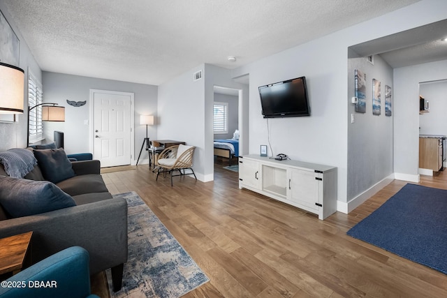 living room with a textured ceiling, light wood finished floors, visible vents, and baseboards