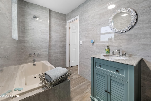 full bath featuring wood finished floors, vanity, tile walls, and a tub