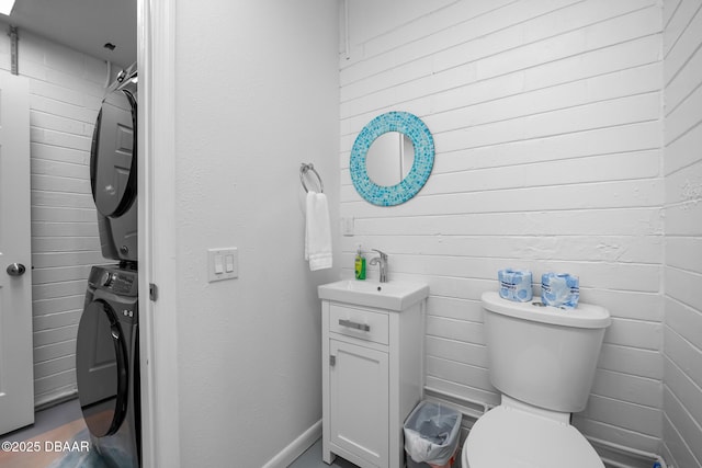 half bathroom with toilet, vanity, and stacked washer / drying machine