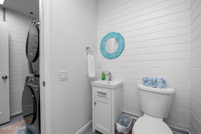 half bath featuring toilet, stacked washer / drying machine, and vanity