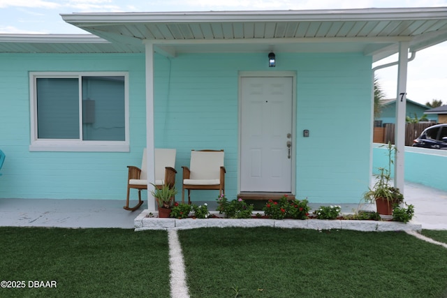 view of exterior entry with fence and a lawn