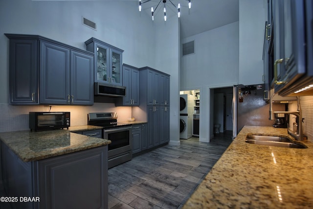 1948 Spruce Creek Lndg, Port Orange, FL 32128 - kitchen featuring a sink, stacked washer / drying machine, stainless steel appliances, blue cabinets, and a high ceiling