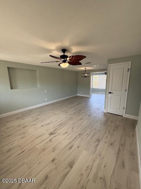 empty room featuring baseboards, a ceiling fan, light wood-type flooring, and a textured ceiling