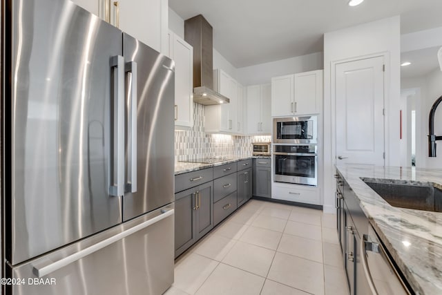 kitchen featuring white cabinetry, wall chimney exhaust hood, stainless steel appliances, light stone counters, and decorative backsplash