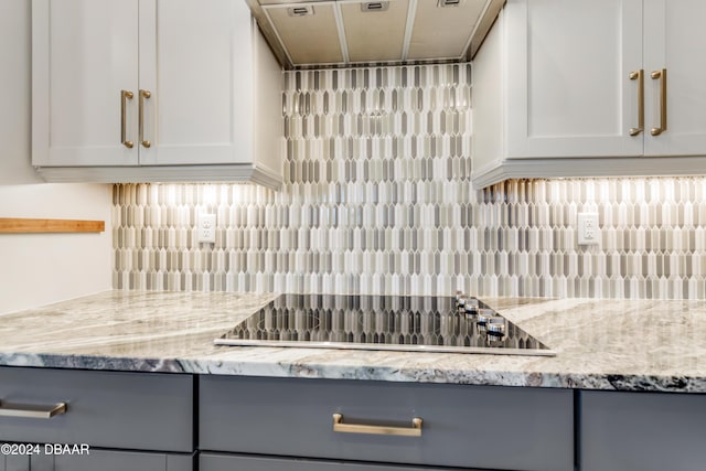 kitchen with gray cabinetry, exhaust hood, black electric stovetop, light stone countertops, and backsplash