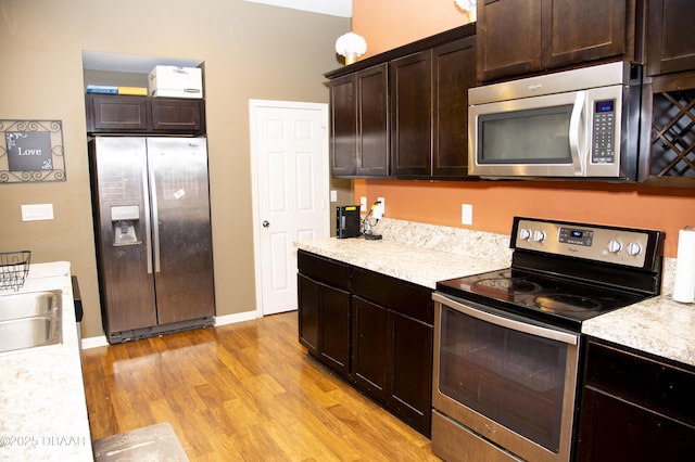 kitchen with a sink, baseboards, dark brown cabinets, appliances with stainless steel finishes, and light wood finished floors