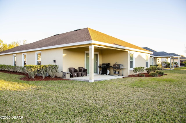 rear view of property featuring a patio, a yard, roof with shingles, and stucco siding