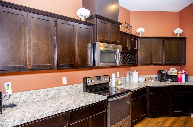 kitchen with dark brown cabinets, appliances with stainless steel finishes, wood finished floors, and light stone countertops