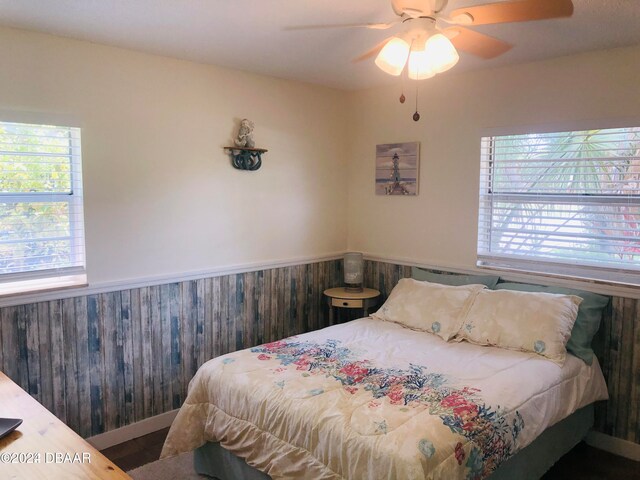 bedroom with ceiling fan, wooden walls, and hardwood / wood-style floors