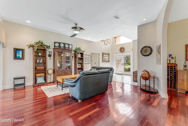 living area featuring ceiling fan, visible vents, arched walkways, wood finished floors, and baseboards