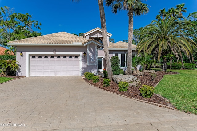 ranch-style home featuring a garage, a tiled roof, stucco siding, and decorative driveway