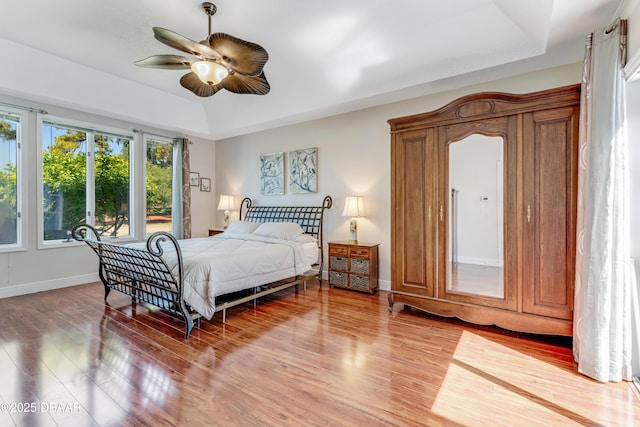 bedroom featuring baseboards, a ceiling fan, light wood-type flooring, and a raised ceiling