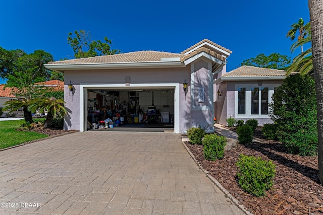 view of front facade featuring an attached garage, decorative driveway, stucco siding, and a tiled roof