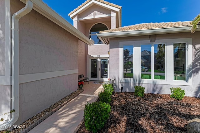 property entrance with a tiled roof, stucco siding, and french doors