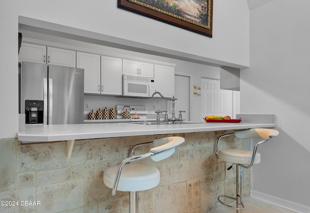 kitchen featuring kitchen peninsula, a breakfast bar area, sink, white cabinetry, and stainless steel fridge